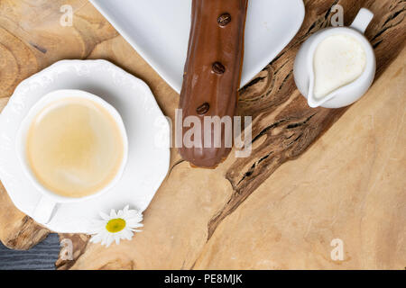 wooden plate with Coffe eclairs with cup of fresh black coffee, pitcher of cream, and coffee beans on Top view. Stock Photo