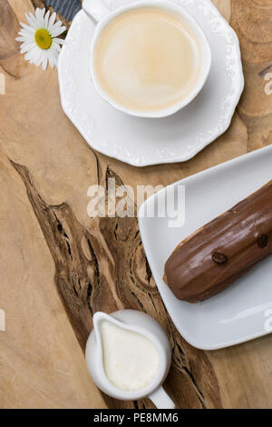 wooden plate with Coffe eclairs with cup of fresh black coffee, pitcher of cream, and coffee beans on Top view. Stock Photo