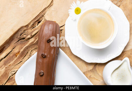 wooden plate with Coffe eclairs with cup of fresh black coffee, pitcher of cream, and coffee beans on Top view. Stock Photo