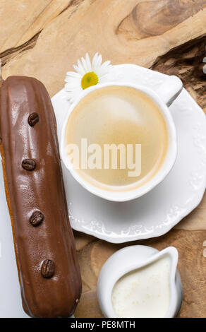 wooden plate with Coffe eclairs with cup of fresh black coffee, pitcher of cream, and coffee beans on Top view. Stock Photo