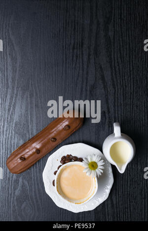 wooden plate with Coffe eclairs with cup of fresh white coffee, pitcher of cream, and coffee beans on Top view. Stock Photo