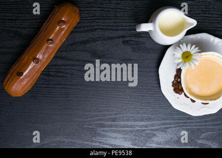 wooden plate with Coffe eclairs with cup of fresh white coffee, pitcher of cream, and coffee beans on Top view. Stock Photo