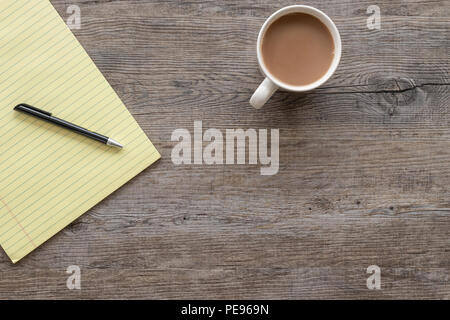 flat lay, wooden table top with mug of tea and yellow legal note pad. Stock Photo