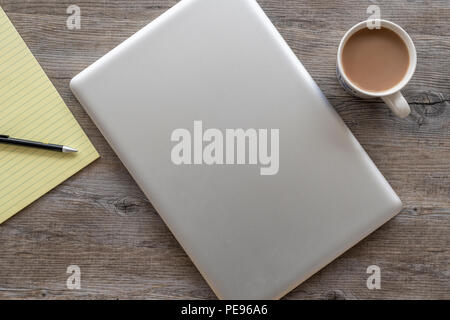 flat lay, wooden table top with laptop computer and yellow legal note pad. Stock Photo