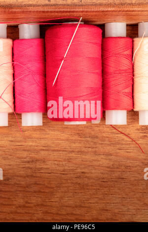 An overhead closeup photo of vibrant red sewing thread spools in a wooden box Stock Photo