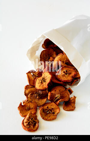 Tasty apple chips wrapped in paper on white wooden background Stock Photo