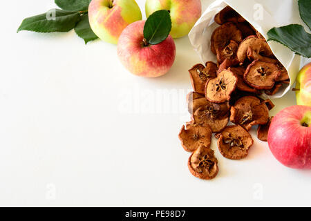 Tasty apple chips wrapped in paper on white wooden background Stock Photo