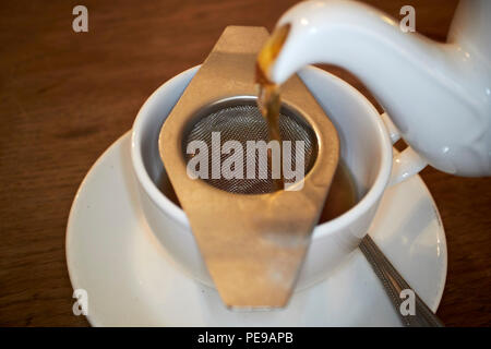pouring tea from a teapot through a tea strainer on a cup of tea in a tea shop in Bath England UK Stock Photo
