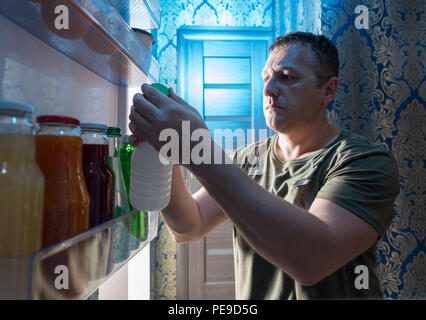 Man selecting something to drink from a fridge holding a white plastic bottle as he stands in the open door viewed from within the appliance Stock Photo