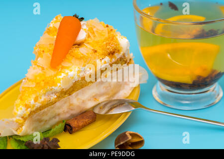 Slice of delicious carrot cake garnished with an orange carrot on creamy icing served with cup of tea over blue Stock Photo