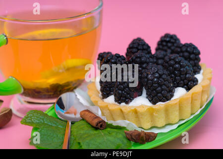 Close-up studio shot of a delicious homemade tart with fresh blackberries served on a saucer with a cup of organic herbal lemon tea Stock Photo