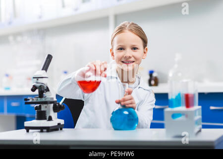 My experiment. Attractive nice cheerful girl using bulbs while posing near microscope and staring at camera Stock Photo