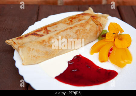 White plate with pancakes pancakes, with jam, cream, fruit and flower on a wooden table Stock Photo