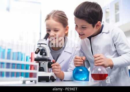Precise look. Jolly energetic curious girl using microscope and smiling while boy holding bulbs Stock Photo