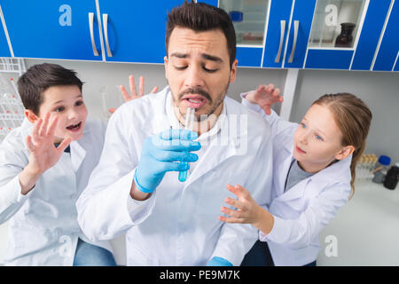 Unexpected outcome. Risky extremal man dressing in gloves and preparing to try liquid while pretty kids preventing this Stock Photo