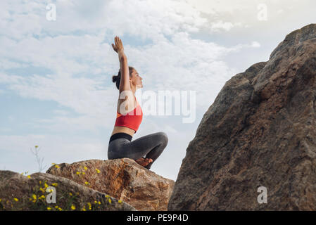 Beautiful young woman doing yoga sitting on rock Stock Photo