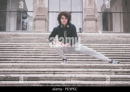 Handsome young sportsman stretching and warming-up for training on staircase Stock Photo