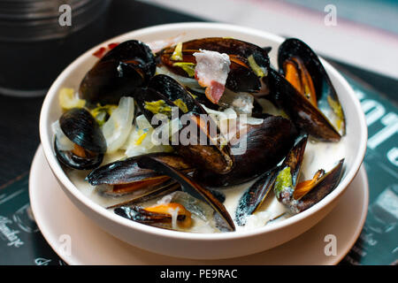 Mussels with onions and bacon in cream sauce in deep plate on the table Stock Photo