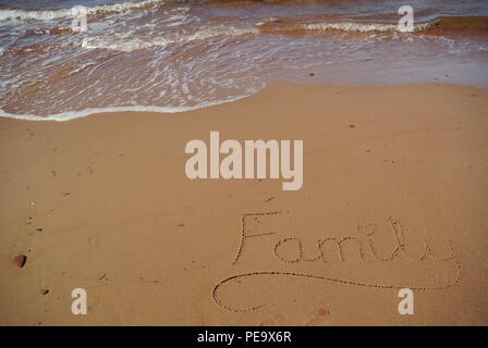 A word 'Family' handwritten on the red sand at the bottom right corner with a foamy wave coming in at the top, Prince Edward Island, Canada Stock Photo