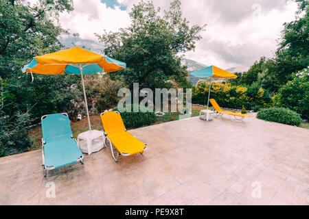 Pair of sun loungers and a beach umbrella on a swimming pool with mountains and clouds in the background. perfect vacation concept. Photo taken in Gre Stock Photo