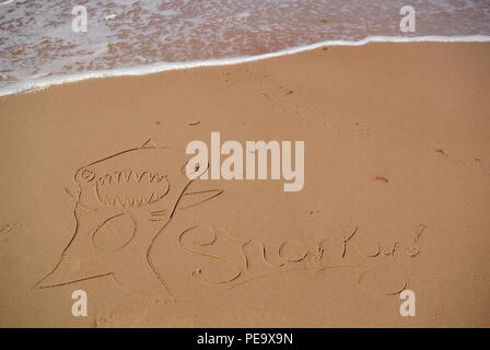 Child's drawing of a shark with a word 'Sharky' written on the red sand on a beach, with a wave in the upper part, Prince Edward Island, Canada Stock Photo