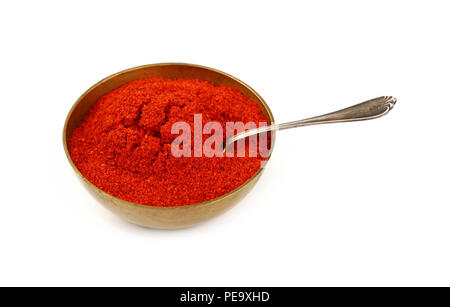 Close up one bronze metal bowl full of red chili pepper or paprika powder with spoon isolated on white background, high angle view Stock Photo