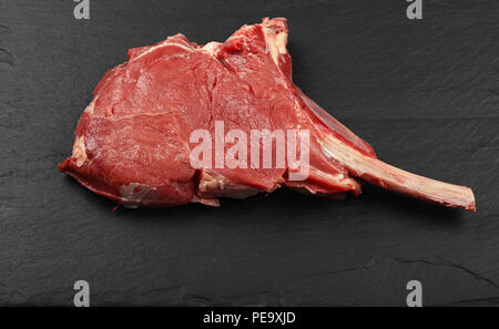 Close up one raw tomahawk ribeye beef steak with rib bone on black slate board background, high angle view Stock Photo