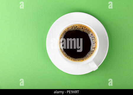 Close up one full white cup of black Americano coffee and saucer over pastel green paper background, elevated top view, directly above Stock Photo