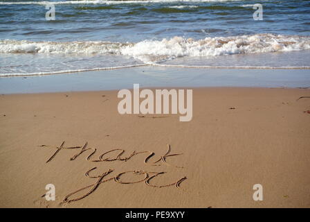 A beautiful gratitude message "Thank you" handwritten on the red sand on a beach with the blue sea and a wave in the upper part, Prince Edward Island Stock Photo