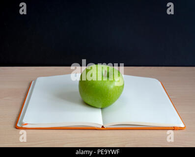 oppen notebook and a green apple in front of blackboard Stock Photo
