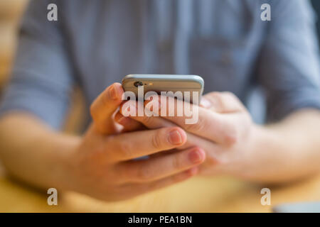 Modern gadget. Selective focus of a modern smartphone being in hands of a nice handsome young man while using it Stock Photo