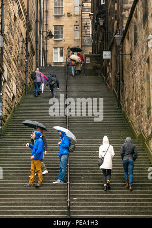 Tourists with umbrellas in rain walking up long steep steps in alley, Warriston's Close, Cockburn Street to Royal Mile, Edinburgh, Scotland, UK Stock Photo