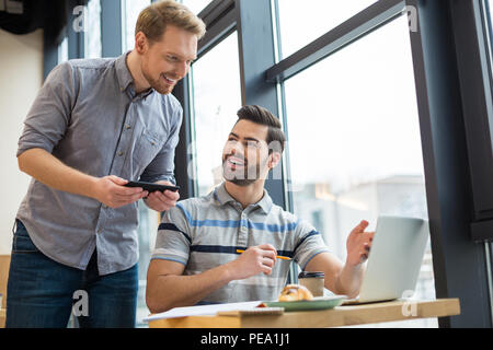 New ideas. Nice pleasant smart men smiling and talking to each other while discussing their idea Stock Photo