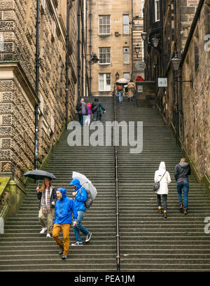 Tourists with umbrellas in rain walking up long steep steps in alley, Warriston's Close, Cockburn Street to Royal Mile, Edinburgh, Scotland, UK Stock Photo