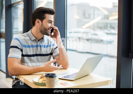 Nice view. Positive pleasant handsome man sitting at the table and talking on the phone while looking into the window Stock Photo