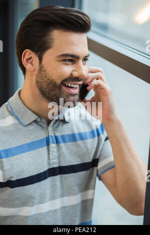 In touch. Happy nice cheerful man smiling and putting phone to his ear while making a call Stock Photo