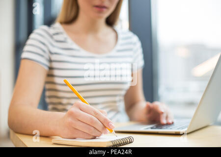 Everyday notes. Selective focus of a small notebook being used by a nice positive young woman for taking notes Stock Photo