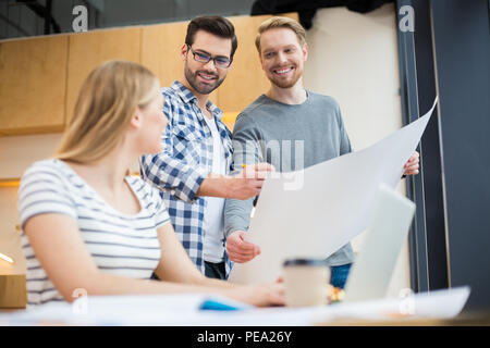Productive teamwork. Positive happy nice man standing together and looking at their colleague while working on a common project Stock Photo