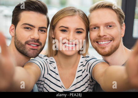 Pleasant memories. Happy cheerful young people standing together and looking at you while taking a photo Stock Photo