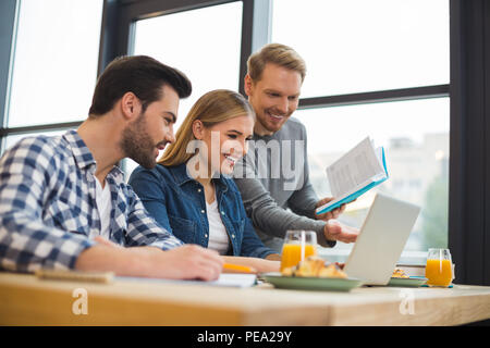 New ideas. Cheerful joyful positive people sitting together and looking at the laptop screen while discussing their startup Stock Photo