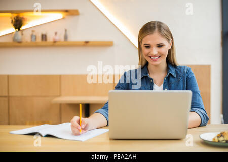 Office equipment. Cheerful nice smart woman sitting in the office and using her laptop while working Stock Photo