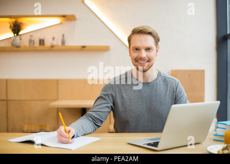 Office worker. Positive joyful nice man smiling and holding a pencil while taking notes Stock Photo