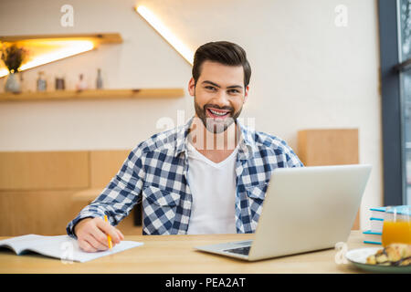 My workplace. Handsome cheerful nice man sitting in front of his laptop and smiling while working in the office Stock Photo