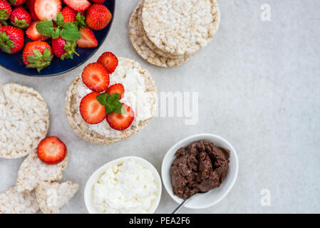 Healthy Snack from Rice Cakes with Ingredients nearby such as Ricotta Cheese, Chocolate Nut Spread and Strawberries on Light Background Stock Photo