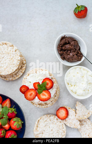 Healthy Snack from Rice Cakes with Ingredients nearby such as Ricotta Cheese, Chocolate Nut Spread and Strawberries on Light Background Stock Photo