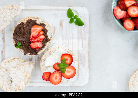 Healthy Snack from Rice Cakes with Ingredients nearby such as Ricotta Cheese, Chocolate Nut Spread and Strawberries on Light Background Stock Photo