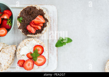 Healthy Snack from Rice Cakes with Ingredients nearby such as Ricotta Cheese, Chocolate Nut Spread and Strawberries on Light Background Stock Photo