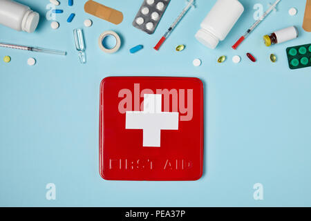 top view of red first aid kit box on blue surface with various medicines Stock Photo