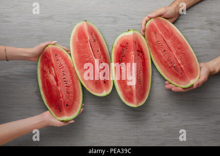 cropped shot of man and woman holding watermelon slices on grey wooden surface Stock Photo