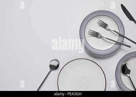 top view of different ceramic plates, forks, spoons and knife on white table Stock Photo